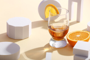 Glass of rum with orange slices, ice cubes and plaster figures on beige background