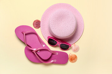Flip-flops with sunglasses, hat and seashells on beige background