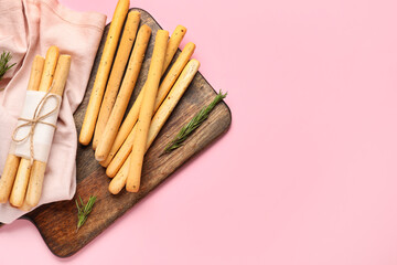 Wooden board with tasty Italian Grissini on pink background