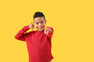 Little African-American boy showing "call me" gesture and pointing at viewer on yellow background