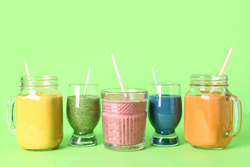 Glasses of colorful smoothie on green background