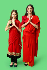 Mother with her daughter in sari praying on green background. Divaly celebration