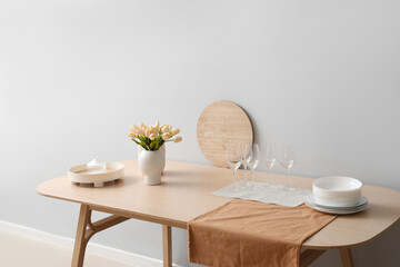 Clean tableware and tulip flowers on wooden table near light wall