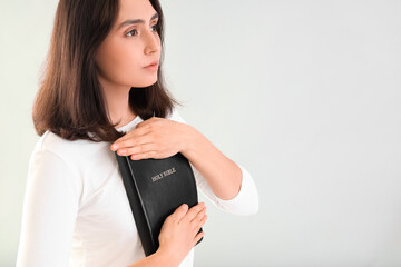 Fototapeta premium Young woman praying with Holy Bible on light background, closeup