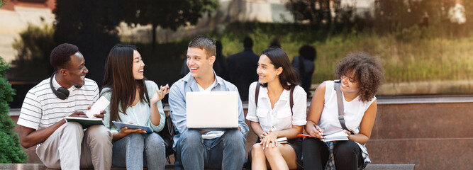 Group Of Multi-Ethnic Students Sitting Outdoors With Laptop, Chatting And Preparring For Classes Together
