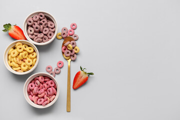 Bowls with colorful sweet cereal rings and cut strawberry on grey background