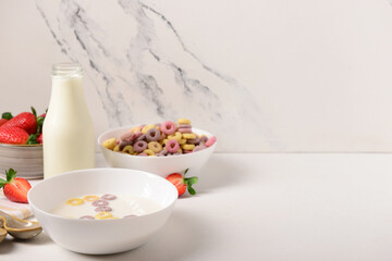 Bowls of colorful sweet cereal rings with milk and strawberries on white background