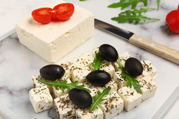 Board with delicious cut feta cheese, black olives and tomatoes on white grunge background