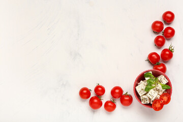 Bowl with tasty cut feta cheese, salad leaves and tomatoes on white background