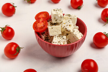 Bowl with tasty cut feta cheese and tomatoes on white grunge background