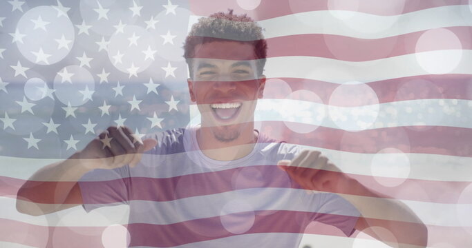 Image of light spots and american flag over happy biracial man dancing on sunny beach - Powered by Adobe