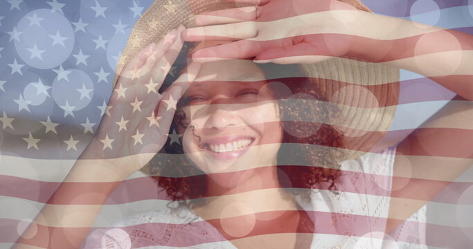 Image of light spots and american flag over biracial woman in sunhat smiling on sunny beach - Powered by Adobe