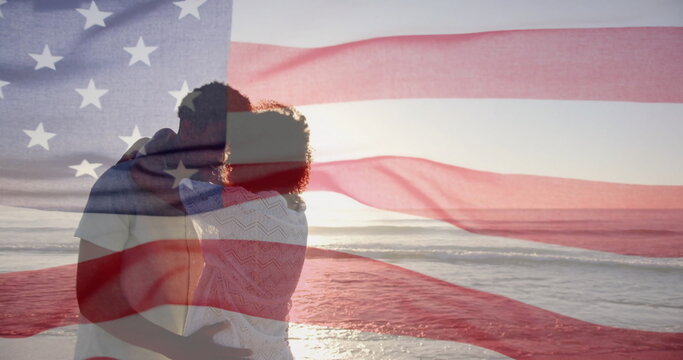 Image of american flag over diverse couple embracing on sunny beach - Powered by Adobe
