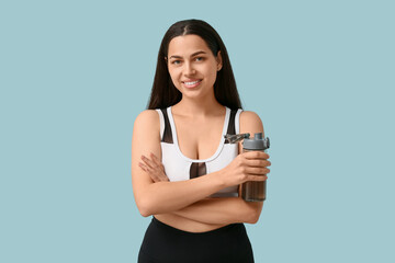 Beautiful young happy woman with sports bottle of water on blue background