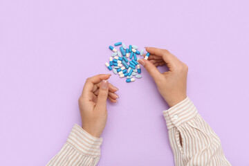 Female hands with different pills on lilac background