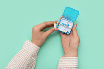 Female hands with pills in case on turquoise background