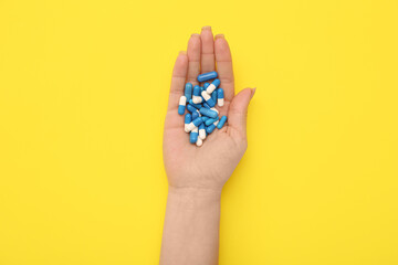 Female hand with pills on yellow background