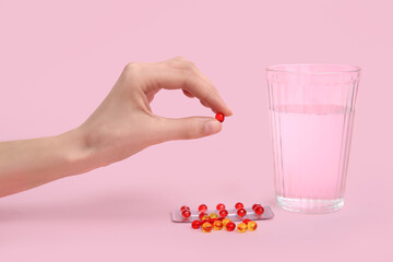 Female hand with pills and glass of water on pink background