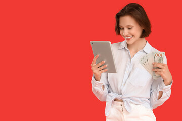 Fototapeta premium Happy young woman with money and tablet computer on red background