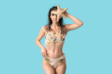 Naklejka premium Beautiful young woman dressed as mythical mermaid with starfish on blue background