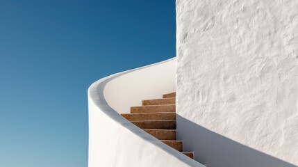 Fototapeta premium An architectural shot of a curved staircase with pristine white walls set against a clear blue sky, emphasizing the graceful lines and minimalist aesthetic.