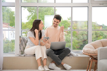 Happy young couple with money and laptop at home