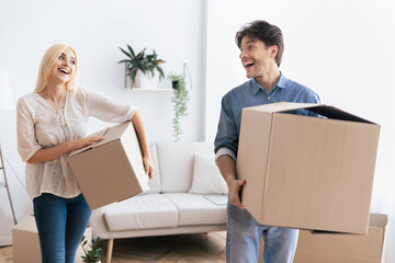A couple happily carries boxes into their new home, smiling and laughing together.