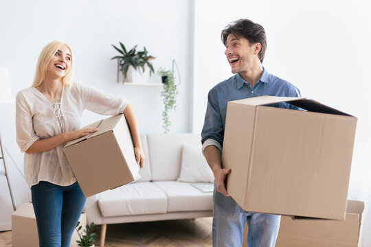 A couple happily carries boxes into their new home, smiling and laughing together.