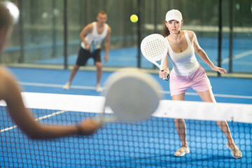 Active woman with racket training on indoor court playing padel game and hitting ball