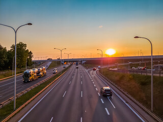 Obraz premium Passenger cars and a car transporter on a multi-line highway in the city at sunset.