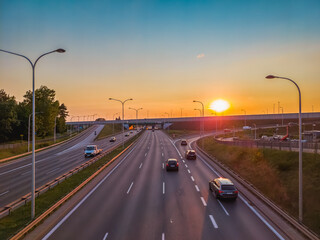 Passenger cars on a multi-line highway in the city at sunset.