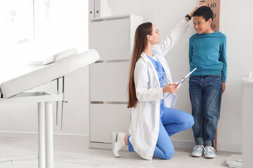 Female pediatrician with little African-American boy measuring height near stadiometer in clinic