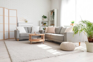 Cozy sofa with cushions, coffee table and folding screen in interior of living room