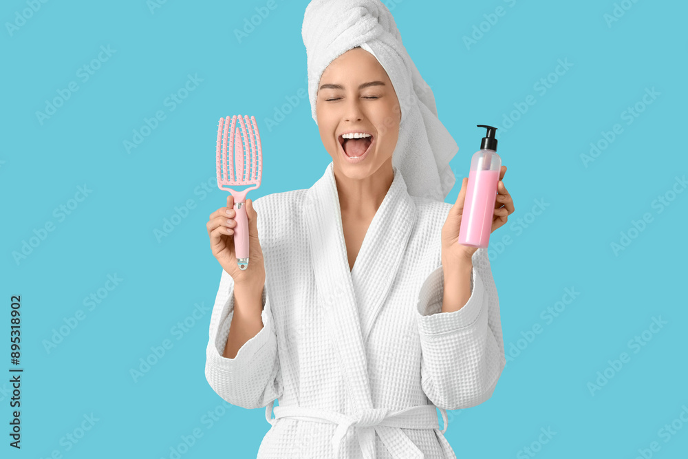 Sticker Beautiful young happy woman in bathrobe with bottle of shampoo and brush on blue background