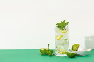 Glass of fresh mojito with juicer and lime on green table against white background