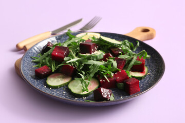Plate of fresh salad with beet and cucumber on lilac background