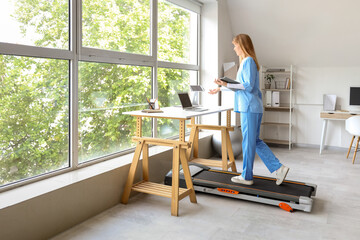 Female doctor with clipboard video chatting on treadmill in clinic