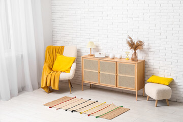 Modern chest of drawers with decor, armchair with plaid, cushion and pouf in room