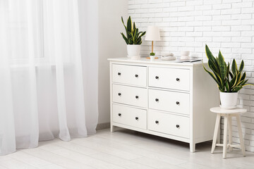 Stylish chest of drawers with decor and plants near white brick wall in room