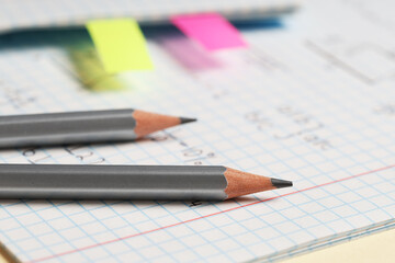 Copybook with handwritten maths formulas with pencils on yellow background, closeup