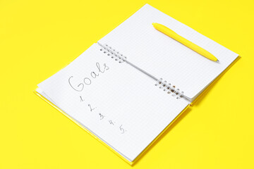 Notebook with list of goals and pen on yellow background