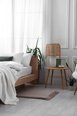 Stylish living room interior with bed, bedside table, lamp and houseplants