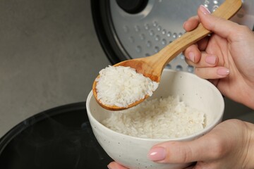 Woman taking boiled rice into bowl on grey background, closeup