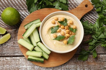 Tasty hummus with chickpeas in bowl and fresh products on wooden table, flat lay