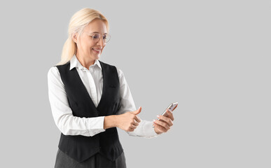 Mature businesswoman unlocking mobile phone on light background