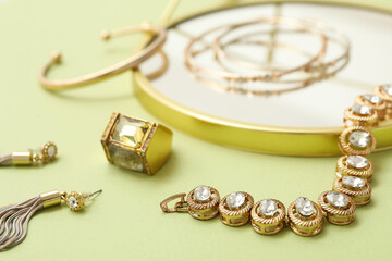 Golden bracelet with precious stones and different jewelry on green background. Closeup