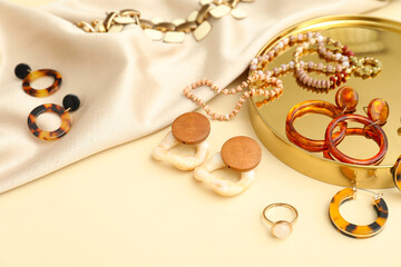 Different jewelry on golden podium with piece of cloth on beige background. Closeup