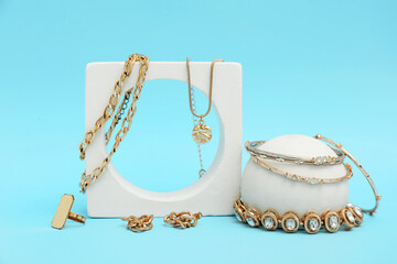 Decorative podium with golden jewelry on blue background. Closeup