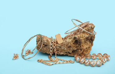 Piece of stone with golden jewelry on blue background. Closeup