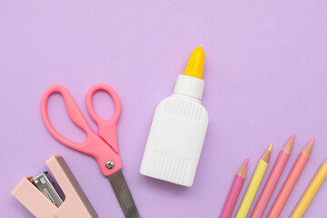 Bottle with glue, stapler and pencils on lilac background. Top view